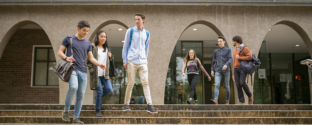 Three students talking as they descend the steps of the Chifley Library.