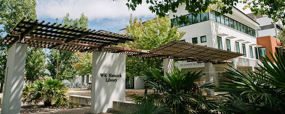 The exterior of the Hancock library is surrounded by lush trees and bathed in sunlight.