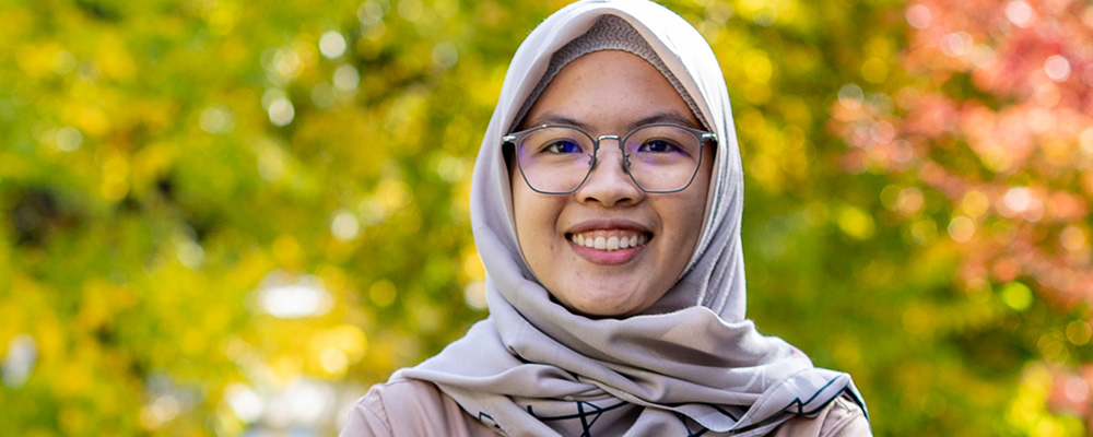 Hasyyati smiling with her arms crossed on the ANU campus.