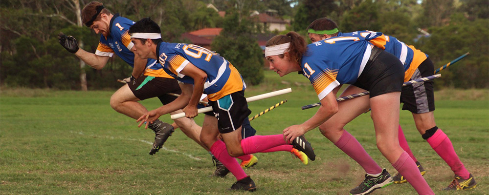 ANU Owls teammates take off flying in a game of Quadball (Quidditch).