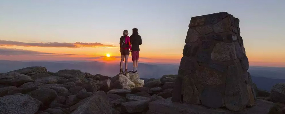Couple watching the sun set at the summit of Mount Kosciuszko in Kosciuszko National Park.