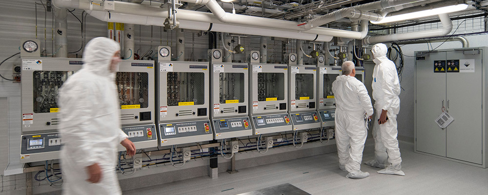 Three men in safety gear stand in front of scientific equipment at the ANU Research School of Physics.