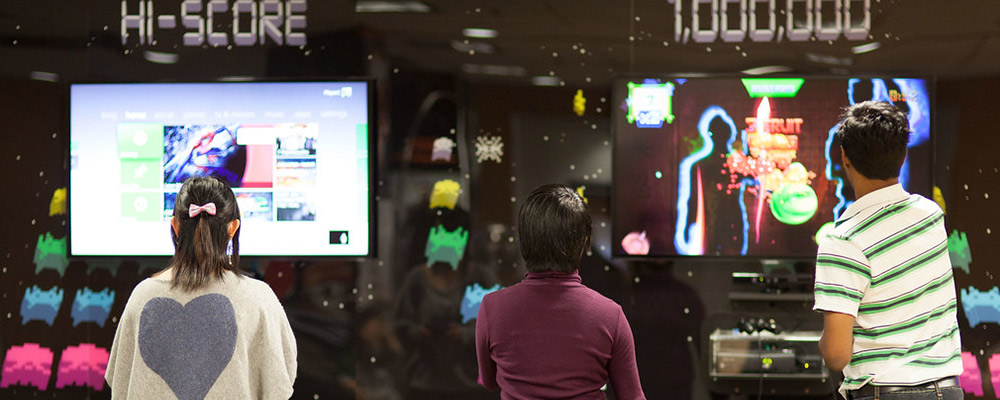Three students playing video games in a gaming lounge.