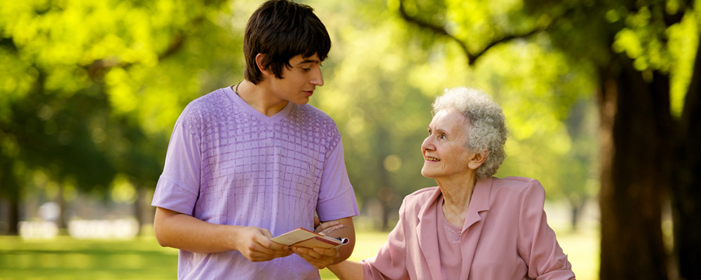 An elderly woman holds the arm of a high school student as he leads her to the shops.