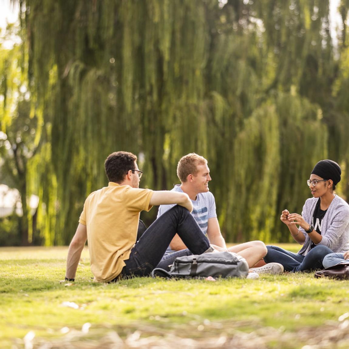 Students sit on grass on ANU campus